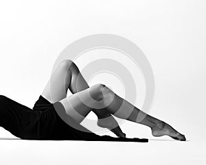 Black and white photo of a woman perfect and naked legs lying on the floor in light black dress on white