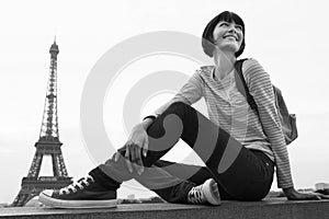 Black and white photo of woman sitting on balcony in front of Eiffel Tower