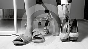 Black and white photo of young businesswoman taking of uncomfortable high heels shoes