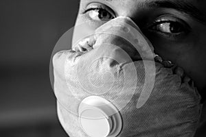 Black and White photo. The young man`s face is covered by a respirator with an exhalation valve. Designed to protect against