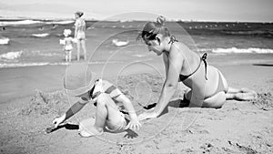 Black and white photo of young mother with her 3 years old child son sitting on the sandy sea beach, playing with toys