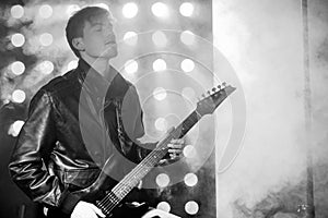 Black and white photo of young rock musician playing electric guitar and singing. Rock star on background of spotlights