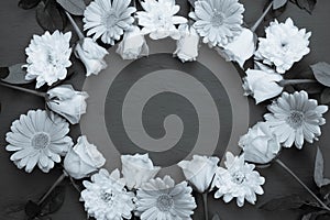 Black and white photo, young roses, gerberas and chrysanthemums are laid out in the form of an oval on a table