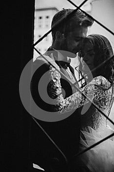 Black and white photo. Young stylish newlyweds are hugging behind old rustic door. wedding day