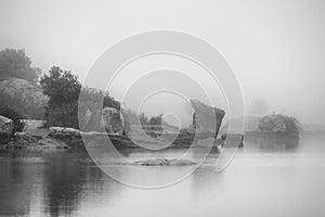black and white photograph of rock formations near water in a foggy lake