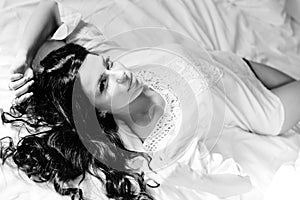 Black white photography of beautiful young woman lying on a bed in pajamas