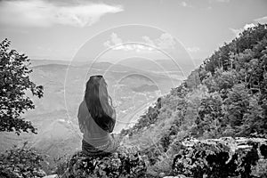 Black and white photography of the girl from the back with black hair sitting on the rock