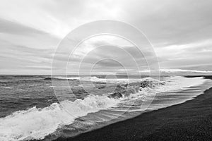 Black and white photography of waves crash ashore on Hvalnes beach in Hvalnes peninsula in Iceland.
