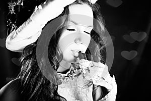 Black and white photography of young beautiful woman in classical clothes eating chocolate with eyes closed, closeup