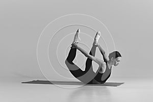 Black and white photography. Young girl with slim fit body training on matt, doing stretching exercises over studio