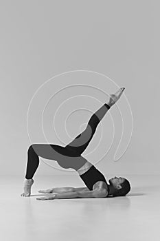 Black and white photography. Young girl with strong slim body doing stretching, training over studio background. Concept