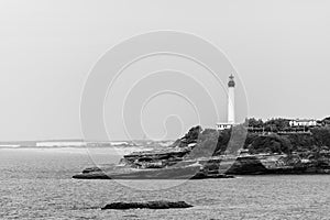 Black and white picture of Biarritz lighthouse on rocks, blurry horizon. Pyrenees-Atlantiques department, French Basque Country