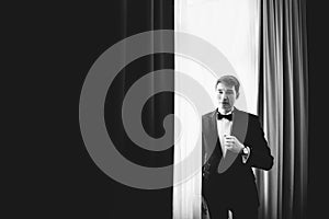 A black and white picture of handsome groom standing behind a wi