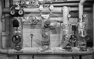 Black-and-white picture of heating pipes in the cellar with shut-off valves, thermometers, valves and throttles, jacket made of