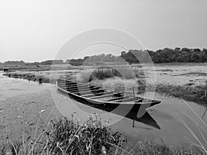 a black and white picture of a wooden boat damped on the river side