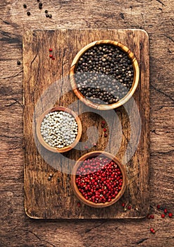 Black, white and pink rose peppers in bowls, assorted spices and spicy herbs on wooden rustic kitchen table, copy space, top view