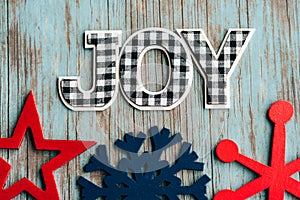 Black and white plaid Joy word letters with blue and red wood snowflakes on a teal wood background, useful for rustic Christmas