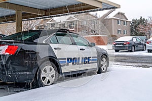 Black and white police car parked in the neighborhood on a snowy and rainy day