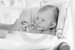 Black and white portrait of adorable baby eating porridge from s