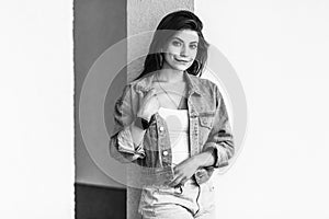 Black and white portrait of beautiful brunette young woman in casual style standing and leaning on wall, standing, holding her