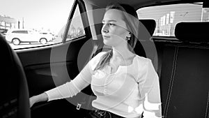 Black and white portrait of beautiful elegant smiling woman sitting on car back seat and looking out of the open window