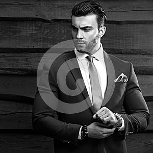 Black-white portrait of beautiful fashionable man in stylish suit against wooden background