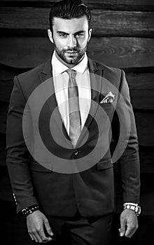Black-white portrait of beautiful fashionable man in stylish suit against wooden background