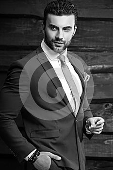 Black-white portrait of beautiful fashionable man in stylish suit against wooden background