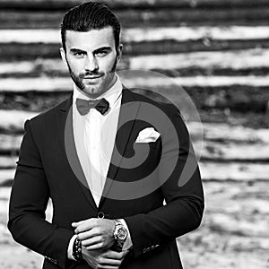 Black-white portrait of beautiful fashionable man in stylish suit against wooden background