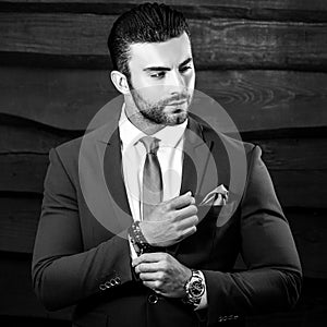 Black-white portrait of beautiful fashionable man in stylish suit against wooden background