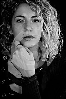 Black and white portrait of a beautiful young woman with blonde curly hair looking worried with her hand placed on her chin