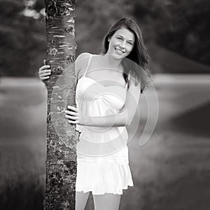 Black and white portrait of a beautiful young woman hugging a tree