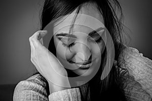 Black and white portrait of a beautiful young woman with long dark hair who shyly looks down while adjusting her hair