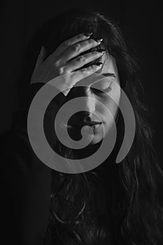 Black and white portrait of a beautiful young woman with long hair who with one hand on her forehead looks sad and desperate