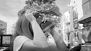 Black and white portrait of beautiful young woman using vintage film camera on street