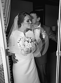 Black and white portrait of bride and groom kissing at hotel room