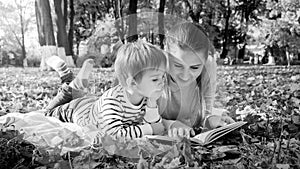 Black and white portrait of family reading story book while lying on ground at park