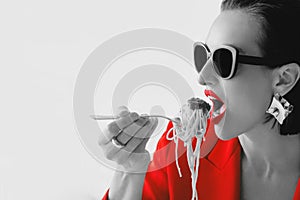 Black and white portrait of fashionable stylish beautiful woman in sunglasses, red jacket eating spagetti pasta.
