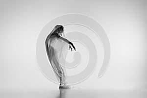 Black and white portrait of graceful ballerina dancing with fabric, cloth isolated on grey studio background. Grace, art