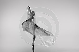 Black and white portrait of graceful ballerina dancing with fabric, cloth isolated on grey studio background. Grace, art
