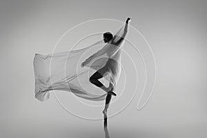 Black and white portrait of graceful ballerina dancing with fabric, cloth isolated on grey studio background. Grace, art