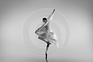 Black and white portrait of graceful ballerina dancing with fabric, cloth isolated on grey studio background. Grace, art