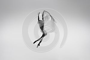 Black and white portrait of graceful ballerina dancing with fabric, cloth isolated on grey studio background. Grace, art