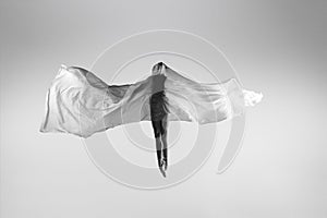 Black and white portrait of graceful ballerina dancing with fabric, cloth isolated on grey studio background. Grace, art