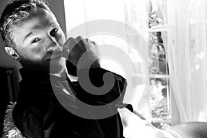 black and white Portrait of handsome man with beard sitting in window with open shirt