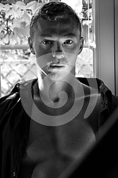 Black and white Portrait of handsome man with beard sitting in window with open shirt revealing pecs