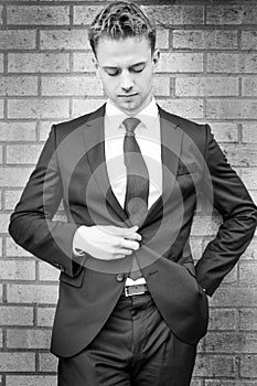 Black and white portrait of handsome man wearing suit standing next to brick wall looking down