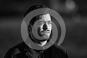 Black and white portrait of a handsome young man squinting his eyes in the winter sun