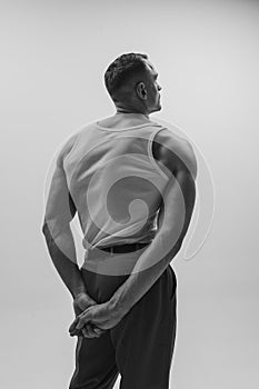 Black and white portrait of muscular man with wide back posing over grey studio background. Masculinity and