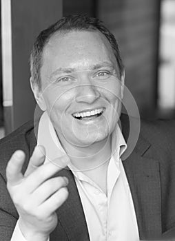 Black and white portrait of a Ñontented and laughing young man in a suit stretching out his hand with an index finger to the fore